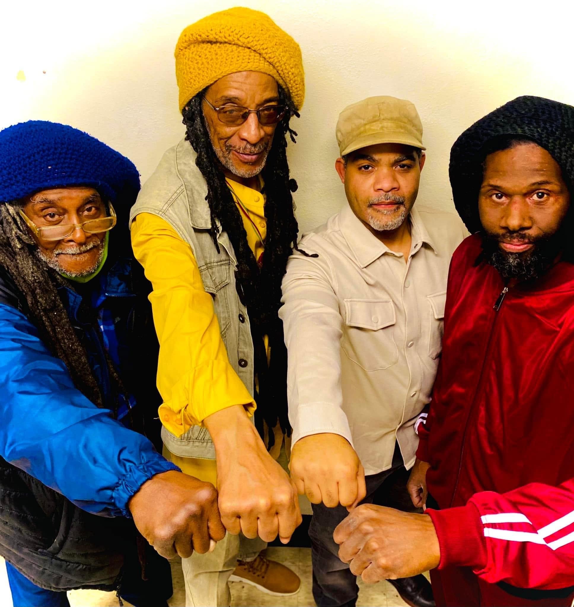 Four members of One Love Reggae Band in red, gold and green tams, arms linked