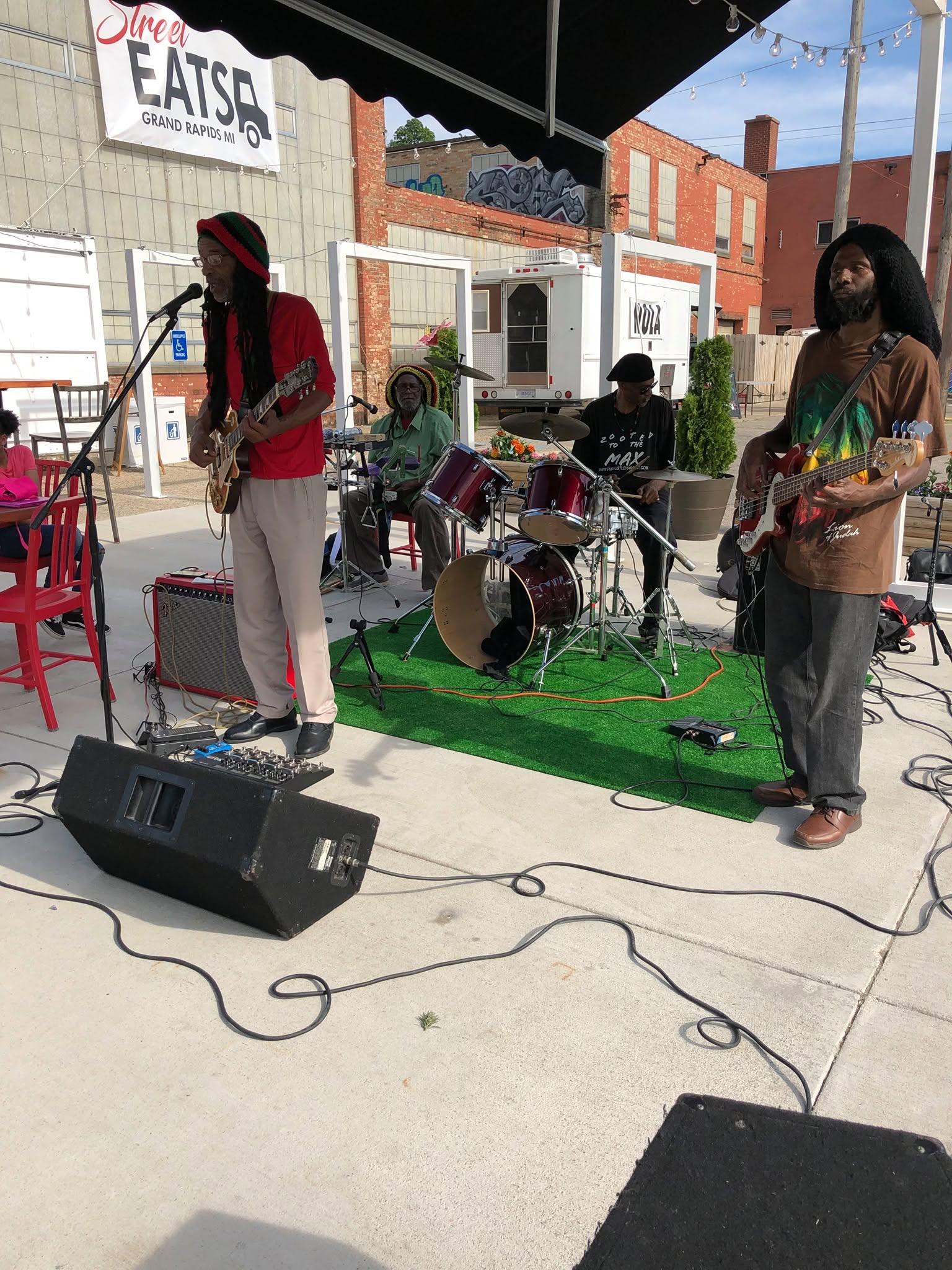 One Love Reggae Band playing an outdoor patio stage for a crowd on the lawn