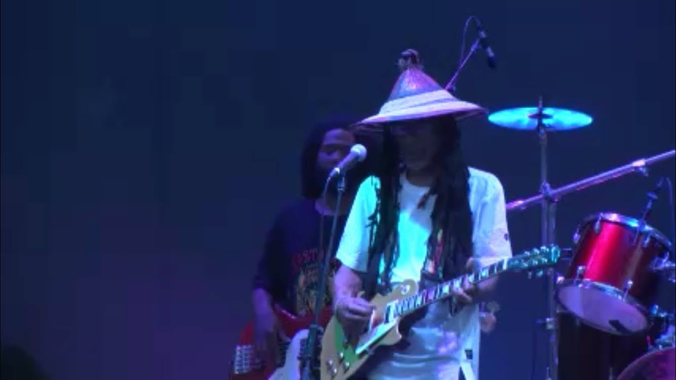 Guitarist in a hat under blue stage lights with the band behind him