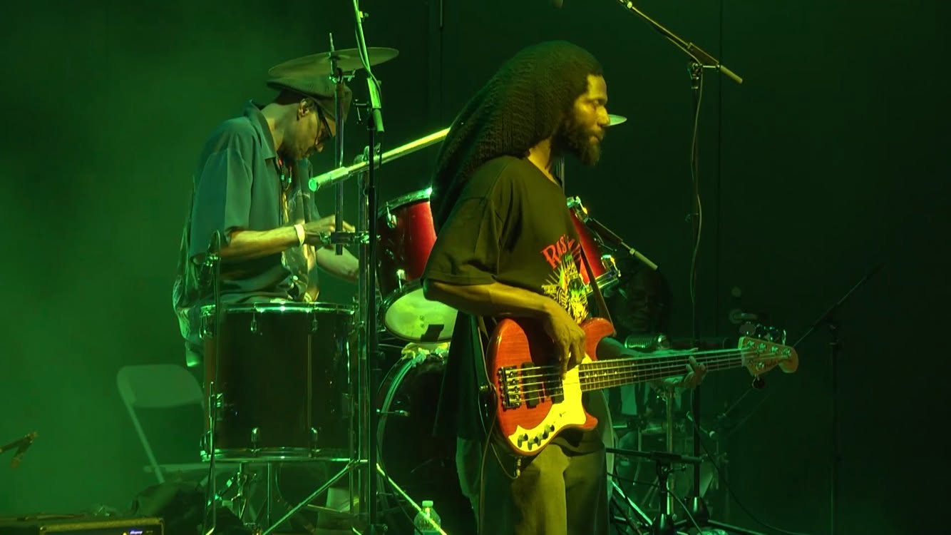 Drummer and bassist performing on a green-lit stage