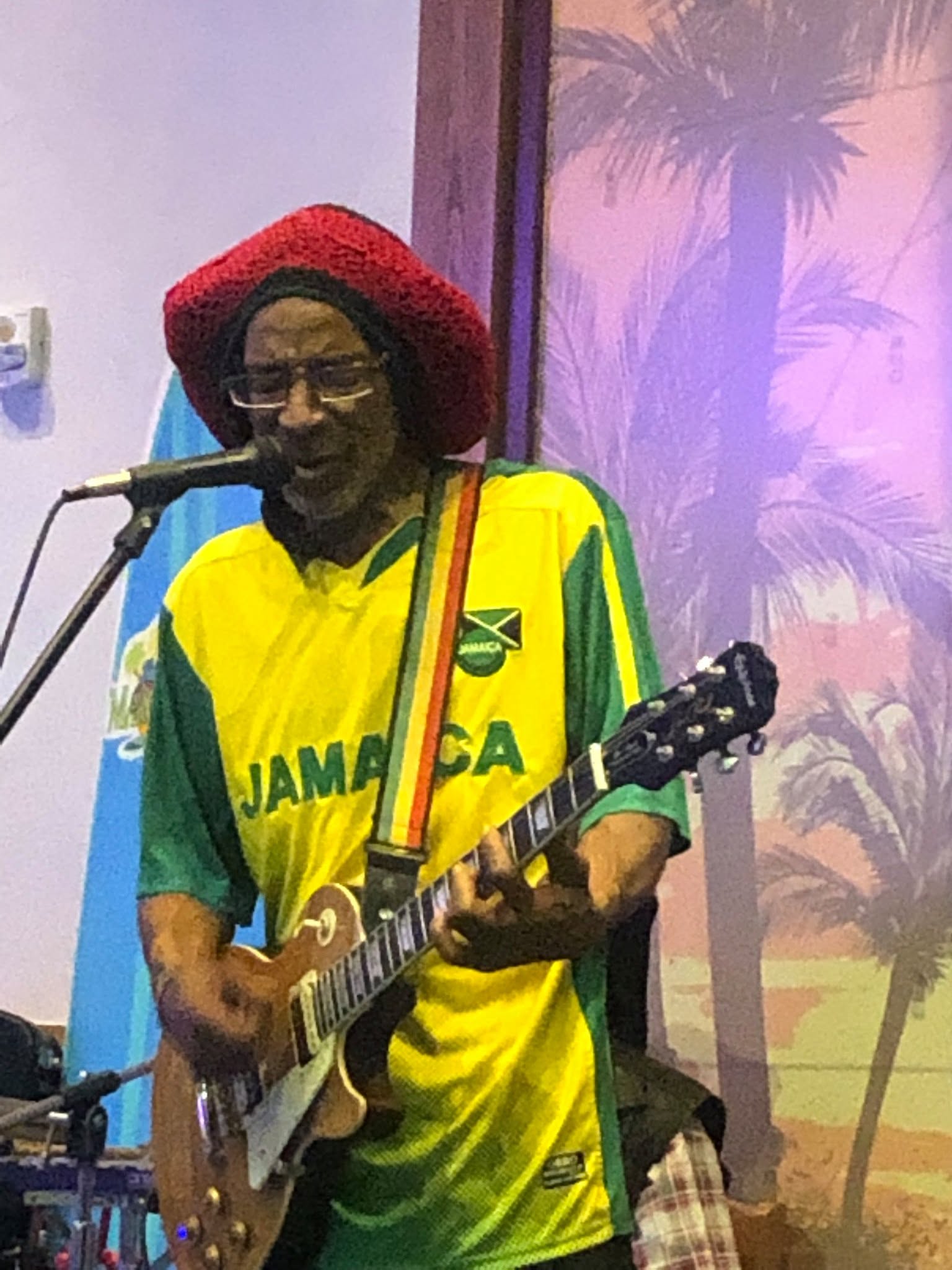 Guitarist in a red tam and yellow Jamaica jersey playing outdoors